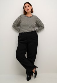 Zwarte high-waisted broeken met een rechte snit, gecombineerd met een gestreept shirt met lange mouwen in zwart en wit. Voorzien van een ronde halslijn en knoopdetails.