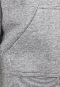 Grå hettegenserstoff med en myk tekstur. Har en kengurulomme og ribbestrikket kant. Materialet ser ut som fleece.