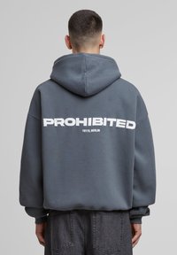 Grey hoodie with a front pocket, featuring large white text "PROHIBITED" and "10119, BERLIN" on the back, made from soft, textured fabric.