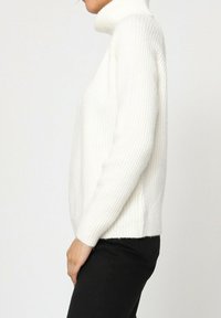 Pull à col montant blanc à côtes avec des manches longues, fabriqué à partir d'un tissu tricoté texturé, présentant une coupe décontractée et un ourlet droit.