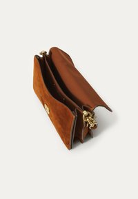 Brun suede håndtaske med en guldbeslag, der har et rummeligt interiør og en kædeaccent. Blød tekstur med strukturerede sider.