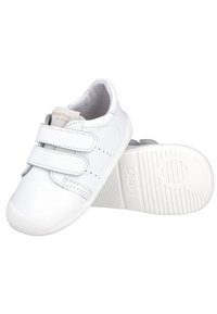 Zapatilla blanca con dos tiras de velcro, detalles perforados y suela de goma texturizada. El interior es gris y cuenta con un forro suave.