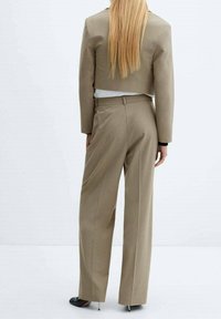Blazer cropped beige et pantalon ample assorti, en tissu lisse. Le pantalon présente une taille haute et des plis subtils.