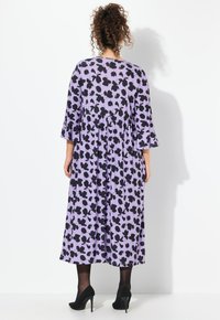 Vestido midi púrpura con un patrón floral negro, mangas acampanadas y cintura fruncida. Combinado con tacones altos negros y medias negras transparentes.