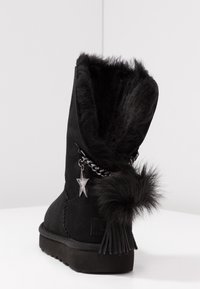 Bottine en daim noir avec une doublure en peluche, un détail chaîne avec un pendentif étoile et un pompon à l'arrière. Semelle plate en caoutchouc.