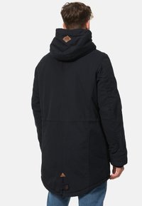 Veste noire à capuche avec un accent triangulaire en cuir dans le dos, fabriquée en tissu texturé avec une coupe légèrement ample.