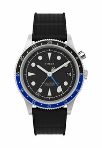 Zegarek Timex Waterbury GMT z czarną tarczą, srebrną stalową kopertą, niebiesko-czarnym pierścieniem oraz teksturowanym czarnym paskiem z gumy.