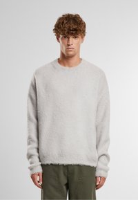 Hellgrauer Pullover aus weichem, strukturiertem Material. Er hat einen runden Halsausschnitt und gerippte Bündchen, mit einem lockeren Schnitt.