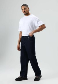 Witte t-shirt met korte mouwen gecombineerd met donkere denim jeans met lichte stiksels en een ruime pasvorm. Zwarte plateau schoenen met gekleurde veters.