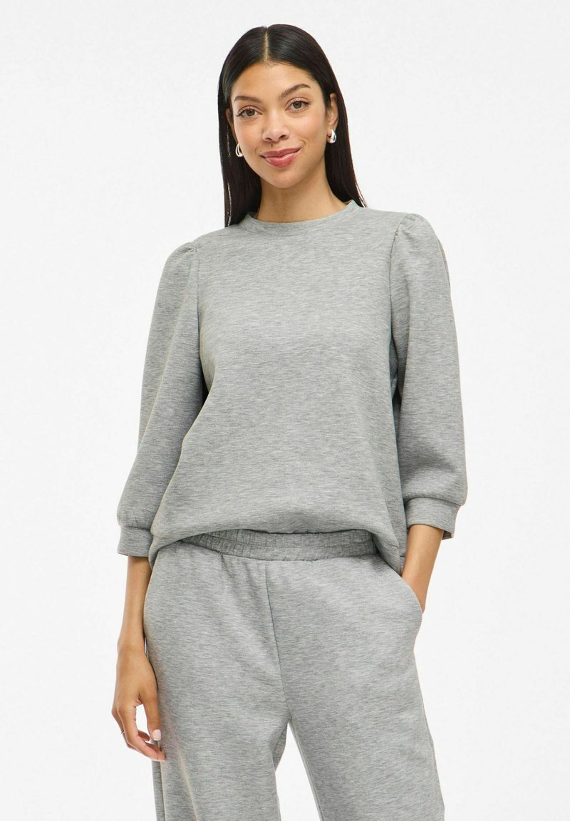 Grauer Pullover mit Dreiviertel-Puffärmeln und Rundhalsausschnitt. Weicher Stoff mit bequemer Passform, kombiniert mit passenden grauen Jogginghosen.