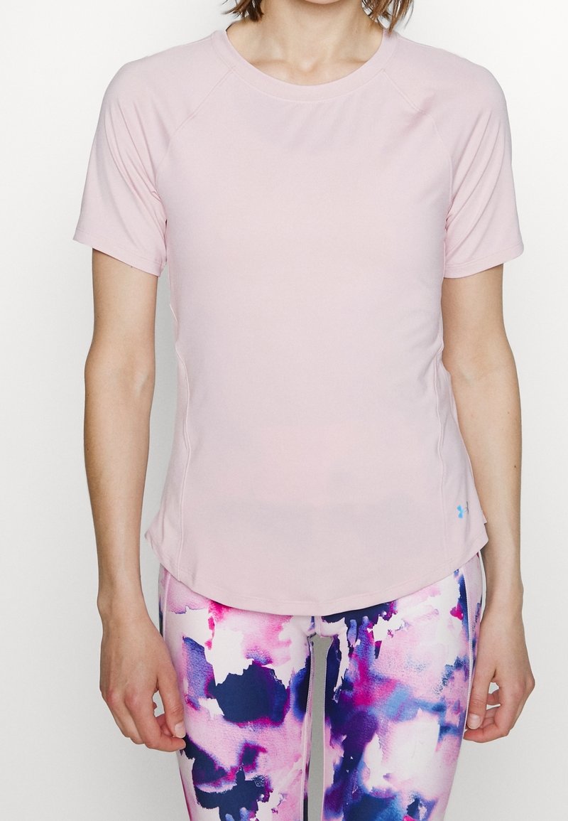 Camiseta deportiva de color rosa claro con mangas raglán cortas, textura suave, dobladillo ligeramente curvado, combinada con leggins coloridos y estampados.
