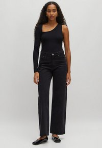 Zwart langslijfs bodysuit met asymmetrische halslijn, gecombineerd met hoge taille zwarte wijde jeans en zwarte ballerina's, tegen een neutrale achtergrond.