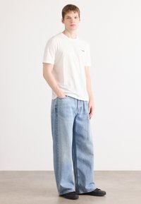 Hvit bomulls t-skjorte med en liten svart logo, kombinert med lyseblå baggy denimjeans og svarte sko. Enkel, uformell antrekk.