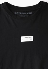 Black t-shirt made of cotton, featuring a round neck. A white tag displays "SHAPE PROJECTS" and product details at the front.