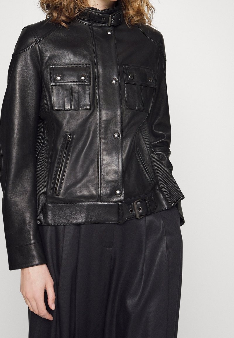 Černá kožená bunda s vysokým límečkem, dvěma náprsními kapsami, bočními kapsami na zip a texturovanými panely v pase. Stříbrné kovové doplňky.