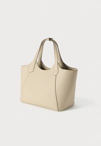 Bēšas ādas tote soma ar divām augšējām rokturiem un izšuvumu detaļām, attēlota uz vienkārša balta fona.