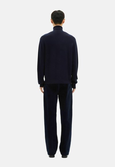 Marineblauer Strickpullover mit Rollkragen und langen Ärmeln, kombiniert mit passenden weiter geschnittenen Hosen. Der Stoff scheint weich und mit einer glatten Textur zu sein.