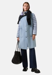 Padded světle modrý kabát s hladkým povrchem, šedými puffery na rukávech, dvěma předními kapsami, v kombinaci s černým šátkem a texturovanou černou taškou.