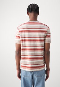 Kortærmet, stribet t-shirt i beige med røde og hvide striber. Blødt bomuldsstof, rund halsudskæring og afslappet pasform.