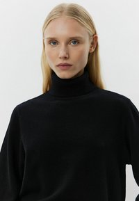 Maglione nero a collo alto con scollatura a costine, realizzato in un tessuto morbido. Presenta una vestibilità rilassata e maniche lunghe. Design minimalista.