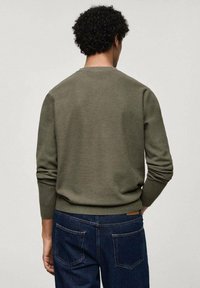 Maglione lavorato a maglia verde oliva con finitura testurizzata, scollo a girocollo e polsini a costine. Indossato con jeans in denim scuro, visto da dietro.