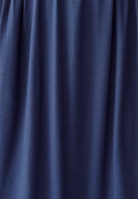 Temno modra tkanina z teksturiranim, tkanim izgledom, ki se ponaša z mehkimi draperijami in subtilnimi svetlobnimi variacijami po površini.