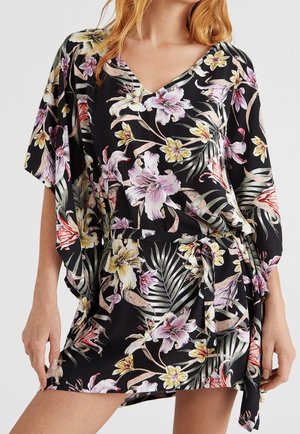 Mujer con vestido negro de flores en escote en V, con flores rosas, amarillas y blancas, y cinturón anudado en la cintura, con las manos apoyadas en las caderas.