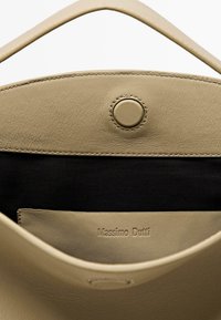 Interiér béžové kožené tašky přes rameno s černou podšívkou. Obsahuje zapínání na cvok a vyražené logo značky na hladkém panelu.