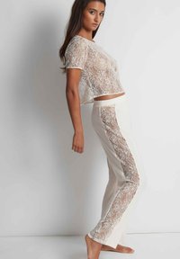 Haut court en dentelle blanche associé à un pantalon crème avec des panneaux latéraux en dentelle. Tissu léger et texturé avec une coupe décontractée.