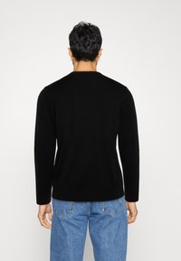 Suéter negro de punto con cuello redondo, manga larga y dobladillo acanalado. La tela parece suave y tiene una silueta ajustada.