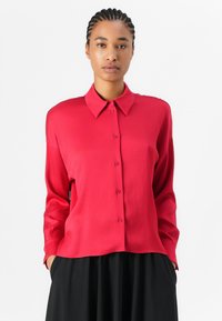 Chemise rouge à boutons, avec col, manches longues et ourlet droit. Texture lisse et design simple qui s'harmonise avec divers styles.