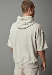 Creme oversized hoodie med snoretræk i huen, korte ærmer og ribbet kant. Glat tekstur og afslappet pasform.