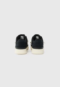 Black suede sneakers with a white rubber sole, featuring a padded ankle collar and dual-tone design, showcasing simple stitching details.