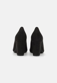 Chaussures à talons aiguilles en daim noir avec un bout pointu et un talon épais, présentant une texture lisse et un design minimaliste. Vue de dos présentée.