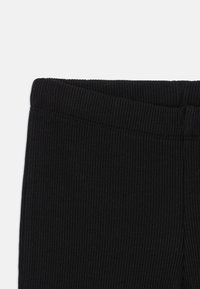 Zwarte geribde legging met een brede tailleband. De stof heeft een textuur met een verticale patroon en biedt gematigde rek voor comfort.