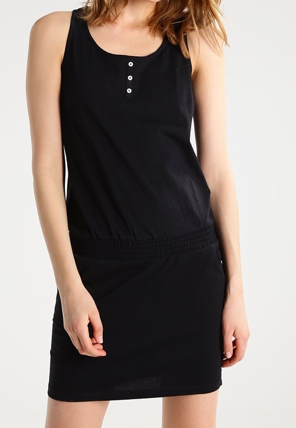 Femme portant une robe noire sans manches avec trois boutons à l'encolure et une taille élastique, debout devant un fond uni.