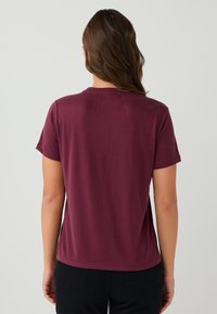 Bordeaux T-shirt met korte mouwen en een ronde hals. Zachte, gladde stof met een ontspannen pasvorm en een rechte zoom.