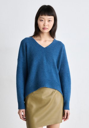 Blue knitted sweater with a V-neck and drop shoulders, paired with a fitted olive green leather skirt. Soft texture and relaxed fit.