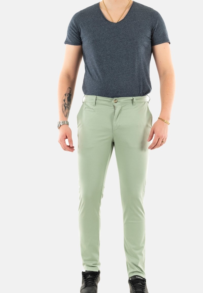 Pantalon slim vert clair en tissu lisse, avec des poches avant et une fermeture à bouton, associé à un T-shirt à manches courtes bleu foncé.