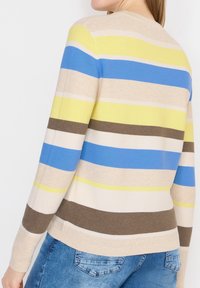 Femme portant un pull en tricot à manches longues avec des rayures horizontales beige, jaune, bleu, blanc et marron, associé à un jean bleu.