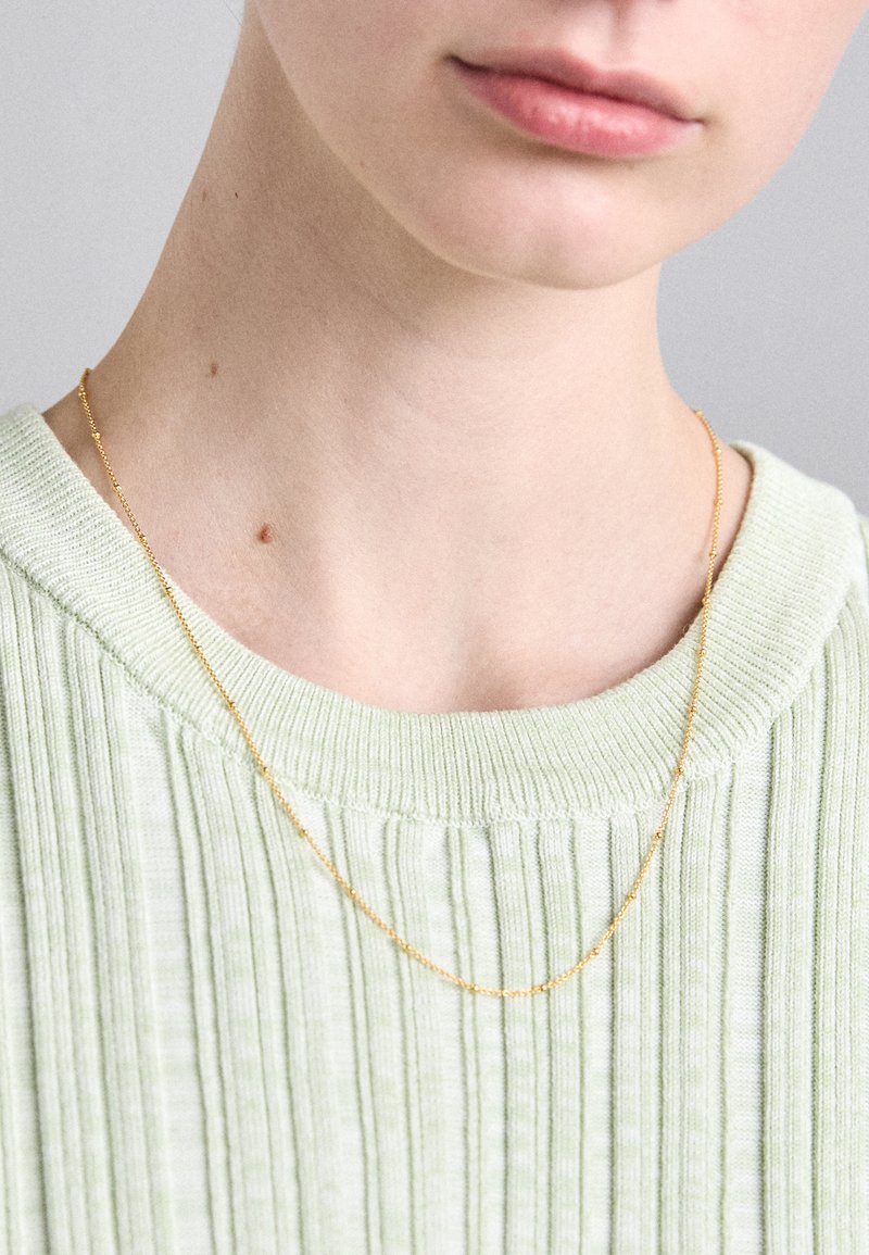 Kuldne kaelakee, millel on helmestik, asetatud kaelale, heledast rohelisest soonik-sweatshirtist ümara kaelusega.