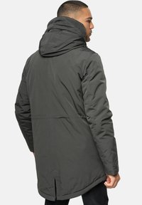 Mørkegrøn, isoleret parka med hætte, der har en lige pasform, synlige sømme og sideslids for øget bevægelighed.