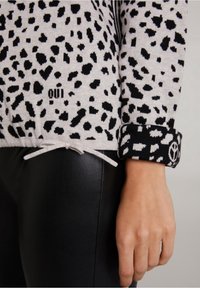 Czarny i biały sweter z nadrukiem w panterkę o teksturowanym wykończeniu, z czarnym mankietem z symbolem pokoju i troczkami u dołu.