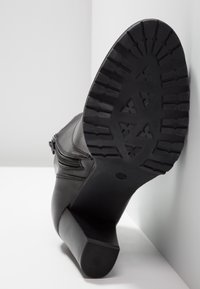 Bottine en cuir noir avec une semelle en caoutchouc crantée, une fermeture éclair latérale et un talon épais. La semelle présente un motif de bande de roulement pour une meilleure adhérence.