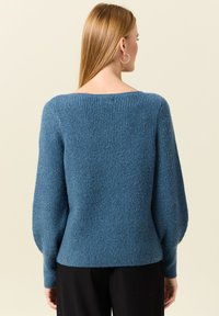 Pull en tricot bleu à coupe ample, texture côtelée et manches bouffantes. Doté d'un large col et d'un matériau doux.