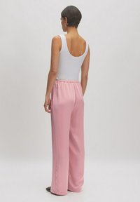 Hellrosa, weite Hosen mit einem elastischen Bund, aus glattem Material gefertigt. Getragen mit einem weißen, enganliegenden Tanktop.