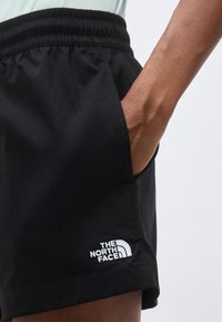 Κοντινό πλάνο του χεριού ενός ατόμου στην τσέπη μαύρων σορτς The North Face με ελαστική μέση.