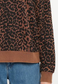 Sweatshirt com estampado de leopardo em castanho e preto, apresentando punhos e barra canelados, com uma textura suave e um corte solto. Combinado com jeans de ganga.