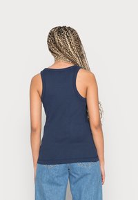 Marinblå figurnära linne med tjocka axelband, ribbad textur och rundad halsringning, kombinerat med ljusblå denimjeans.