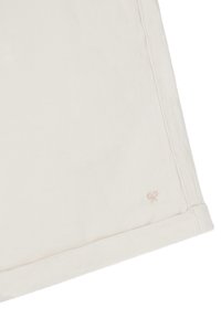 Tela de algodón color crema con una textura suave, que presenta un pequeño diseño de tijeras bordado cerca del dobladillo y un acabado de costura simple.